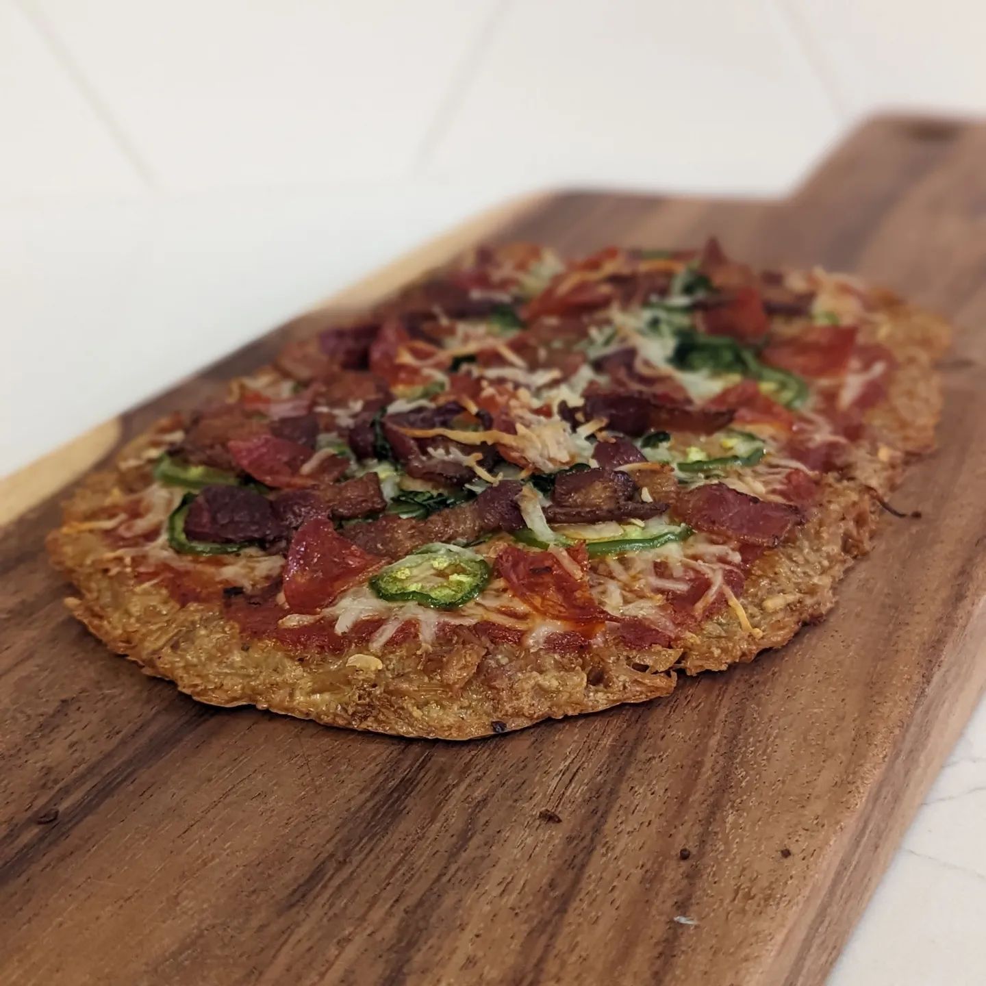 Chicken Crust jalapeno, bacon, pepperoni and Spinach pizzaChicken crust is the absolute best high protein low carb pizza crust (move aside fathead dough). Dry out a can of chicken (Costco cans) in the smoker to add a great smoke flavor and get that chicken nice and dry. Then mix with the chicken 1.5oz Parmesan cheese, 1 tablespoon of almond flour and enough egg to rehydrate the chicken and pull it all together. This crust used two eggs. Form the crust on a parchment lined sheet pressing it nice and thin using a fork. The bake/smoke at 350 for another 15-20 minutes, flip and top with your favorite toppings. I went with @raoshomemade marinara, mozzarella, bacon, jalapeno, spinach and pepperoni. Finished with a little more Parmesan and baked till everything was golden and bubbly. I smoked and cooked this using @bearmountainbbq oak wood for a nice smoke flavor. #chickencrustpizza #lowcarbpizza #fatheaddough #bearmountainbbq #pizzanight